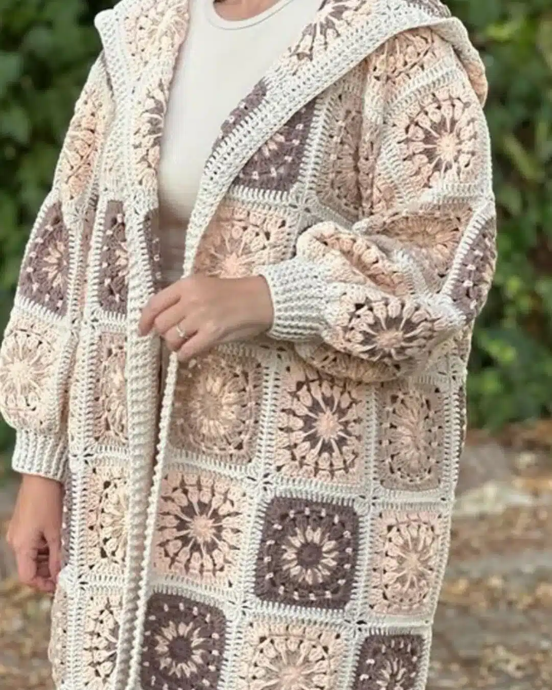 Casaco de crochê com capuz em tons pastel e quadrados decorativos.