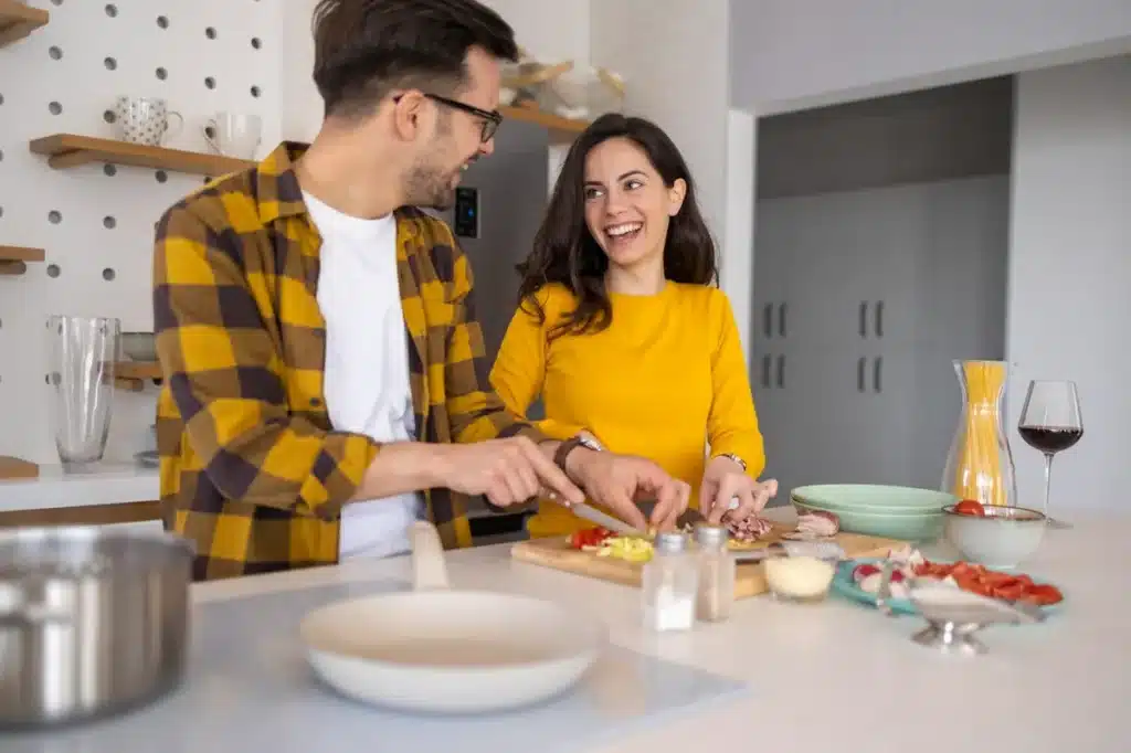 Casal sorridente cozinhando juntos em cozinha moderna preparando ingredientes para jantar