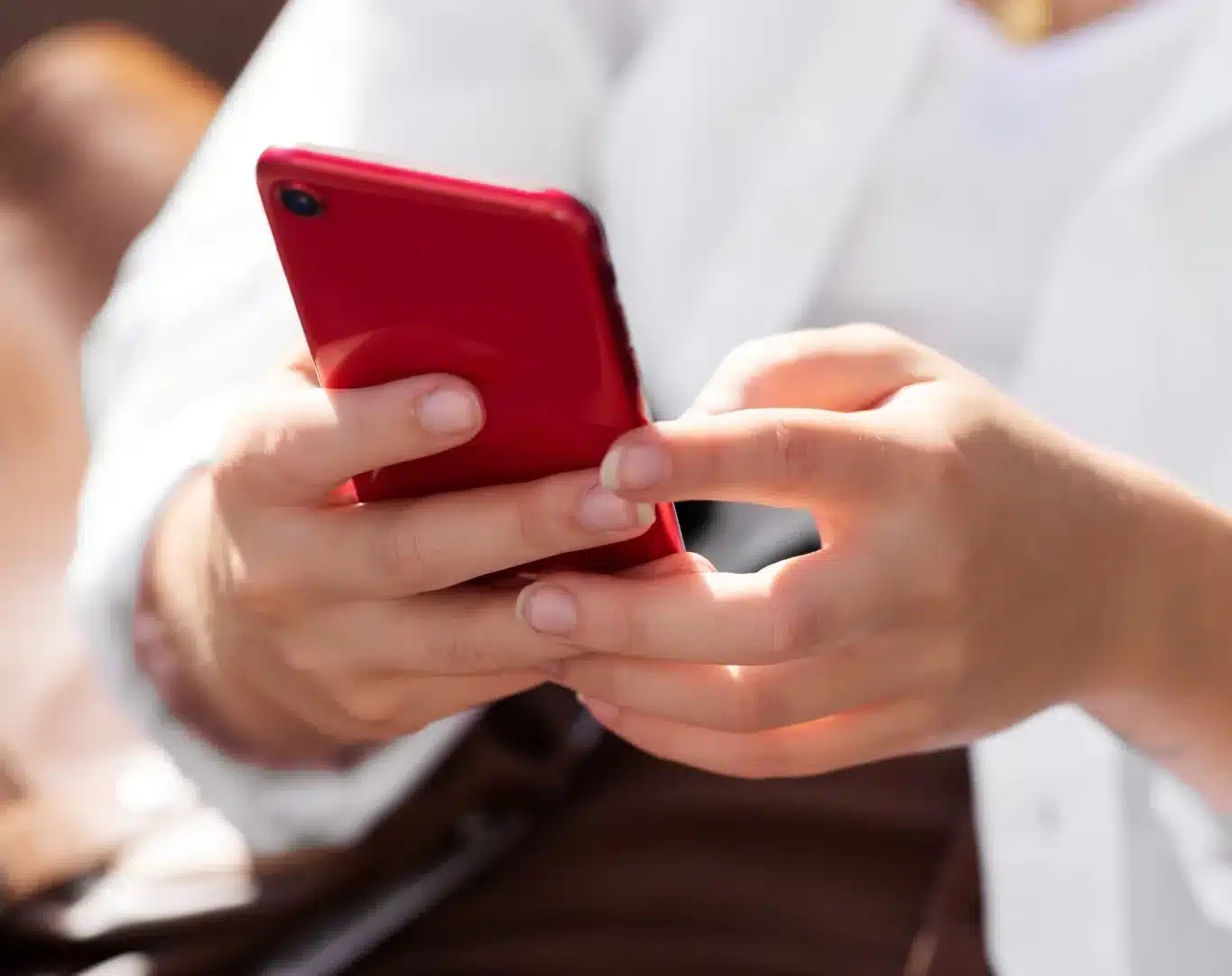 Mulher segurando smartphone vermelho em ambiente ao ar livre, em dia ensolarado.