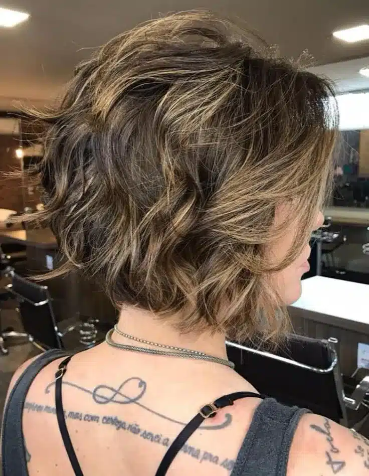 Corte bob desestruturado com ondas e mechas loiras, visto de lado, em um salão de beleza