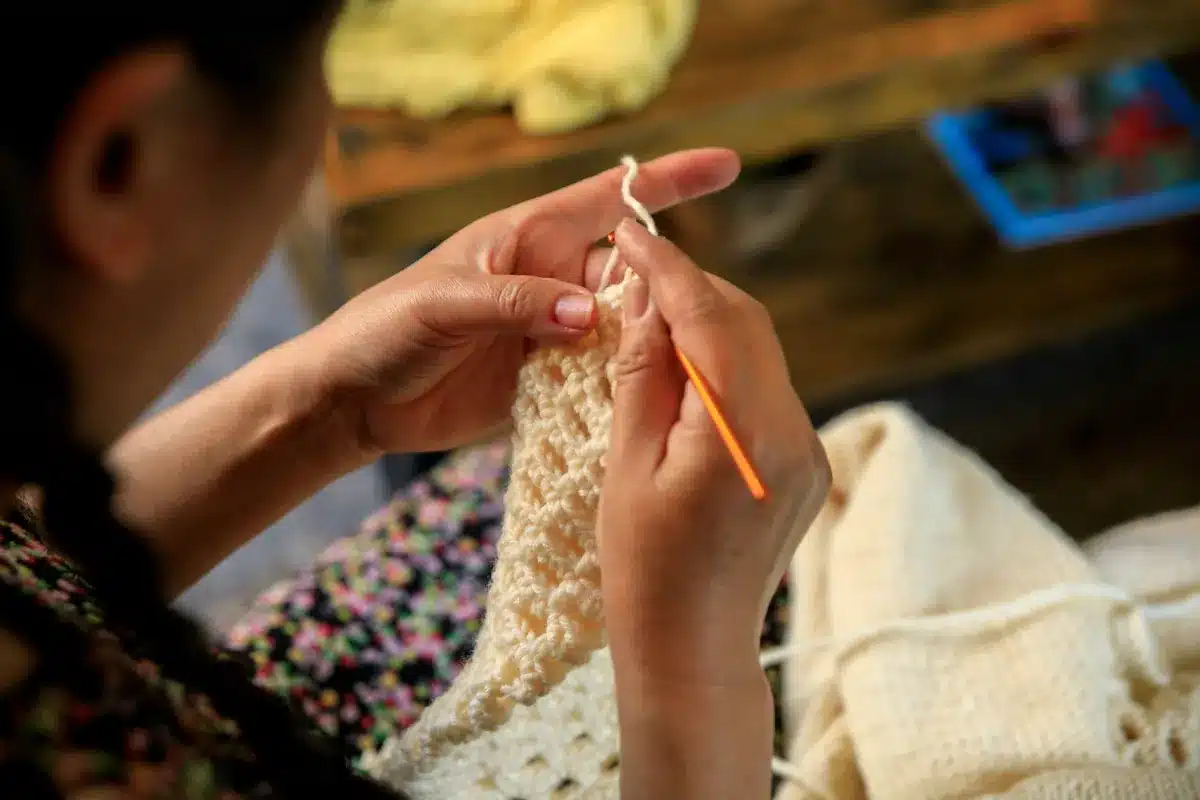Mãos femininas confeccionando peça de crochê com agulha laranja.