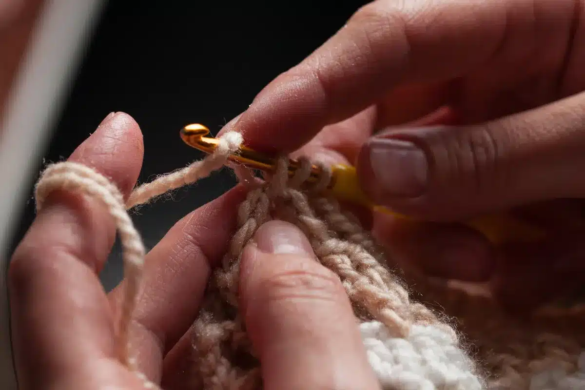 Pessoa fazendo crochê com fio e agulha em tons suaves, focando no trabalho manual.