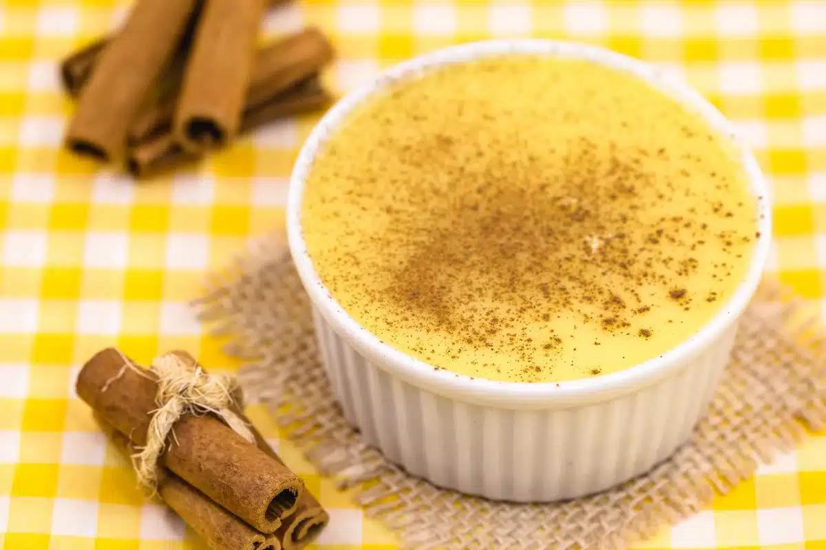 Curau de milho com pó de canela polvilhado sobre ele em fundo de mesa xadrez