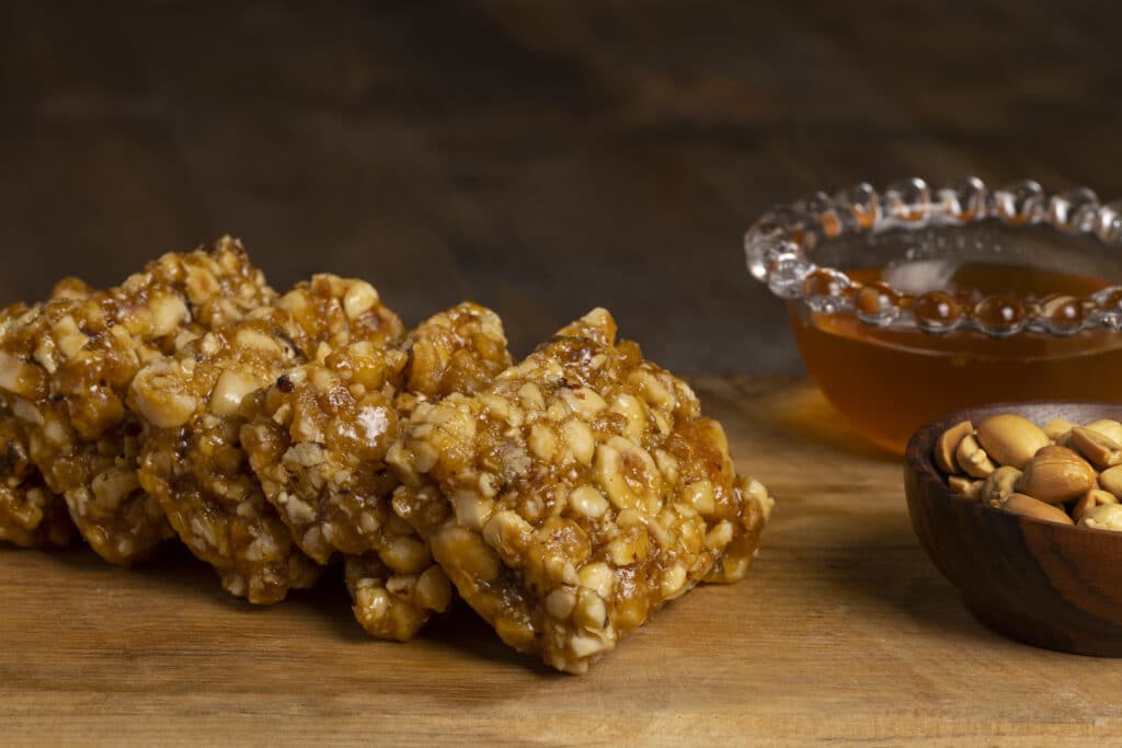 Pedaços de pé-de-moleque com amendoim caramelizado, acompanhados de mel e amendoins em tigela