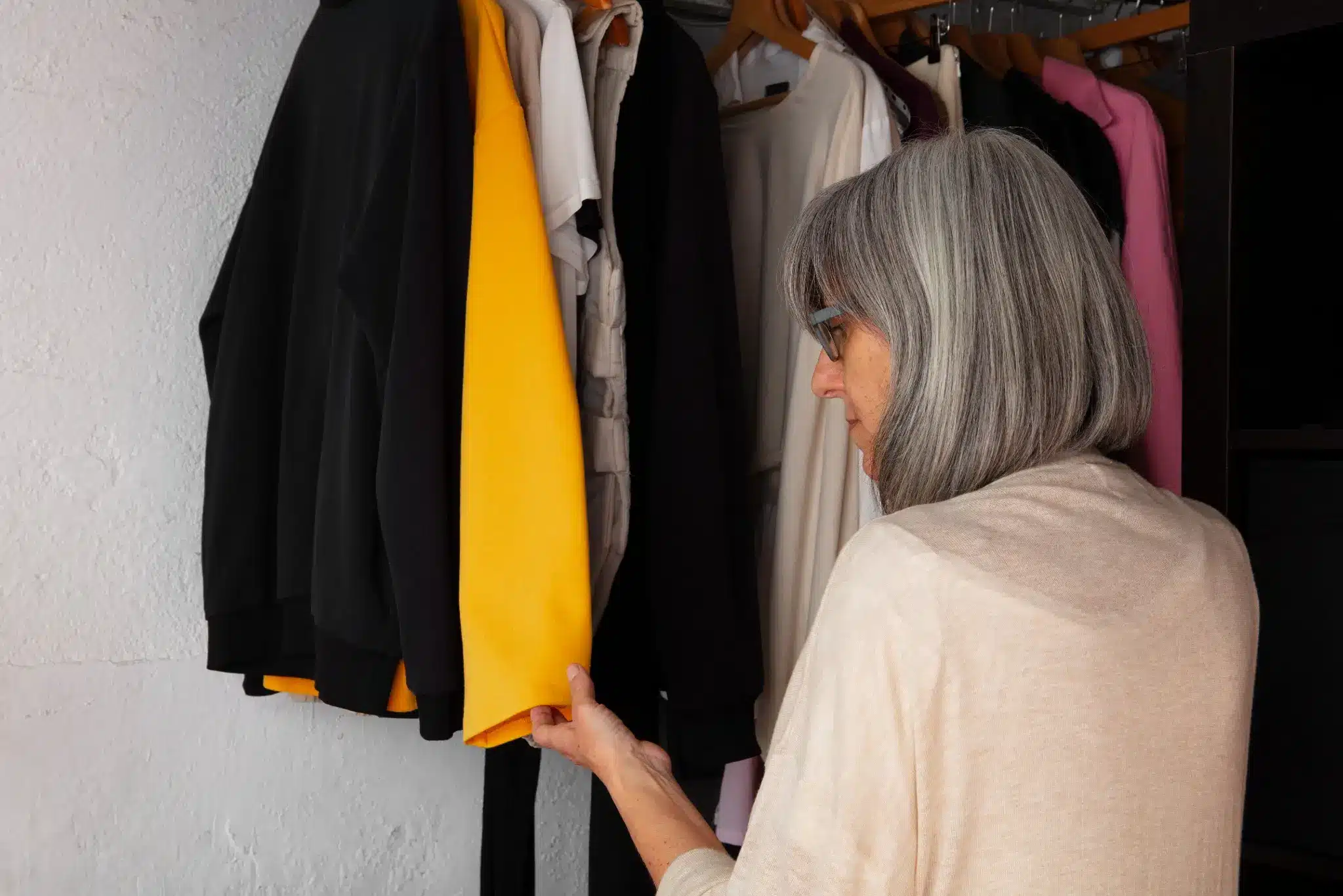 Mulher com cabelo grisalho analisando roupas no armário, com foco em roupas coloridas.