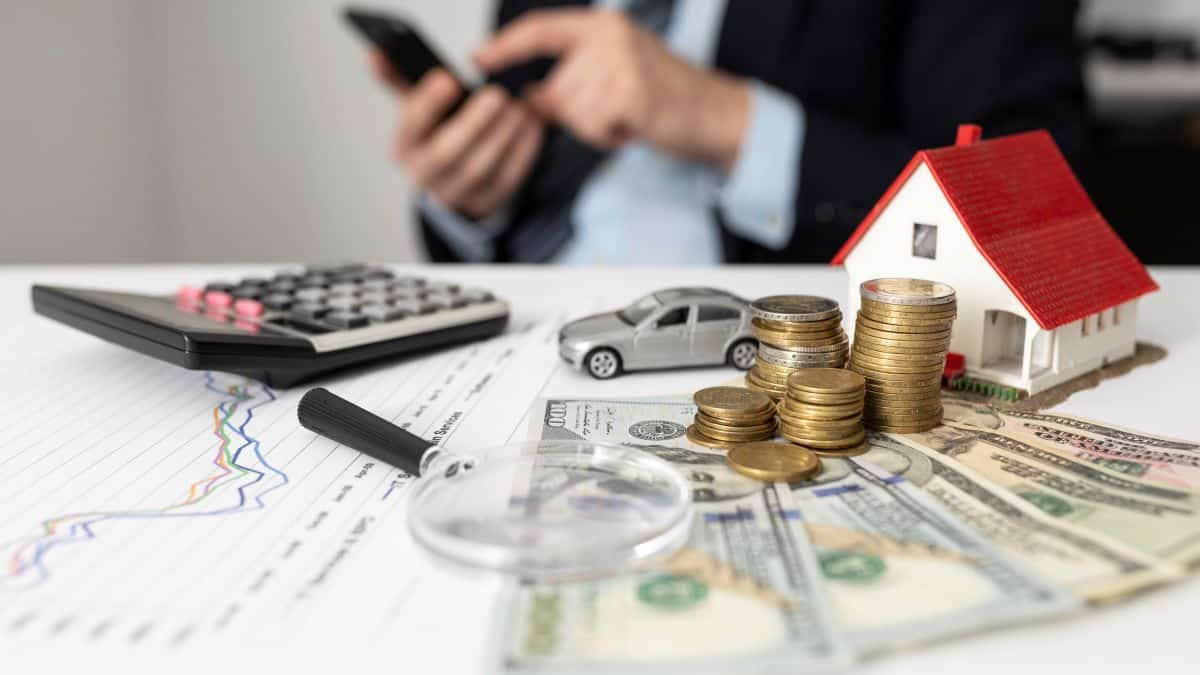 Elementos representando finanças, como moedas, casa em miniatura, carro e calculadora