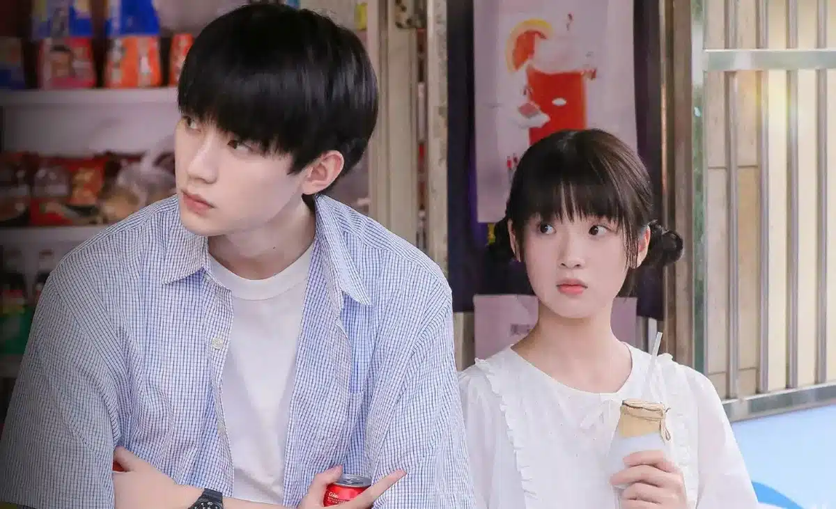 Casal em cena de dorama, com expressões de interesse e curiosidade, em ambiente descontraído.