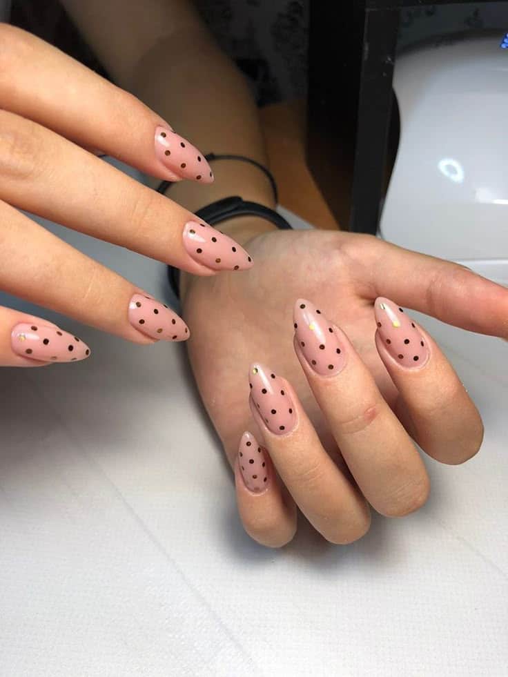 Unhas decoradas com fundo nude e estampa de poás pretos, estilo delicado e moderno.