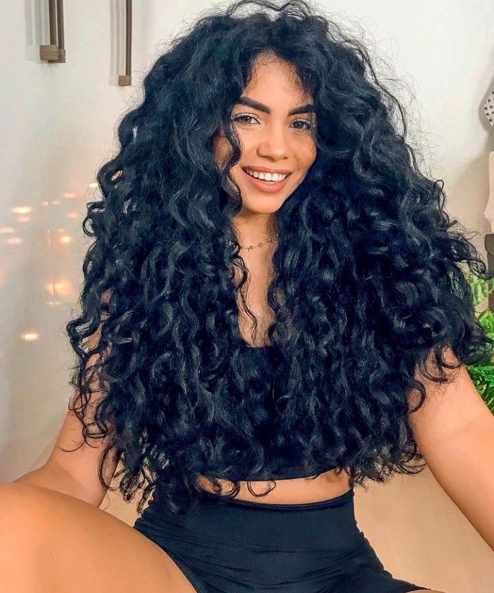 Mulher com cabelo volumoso e cachos definidos, exibindo a tonalidade preto azulado com brilho.