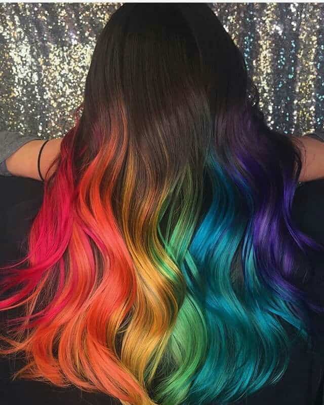 Mulher com cabelo longo e ondulado, exibindo uma coloração vibrante em um gradiente de cores do arco-íris.
