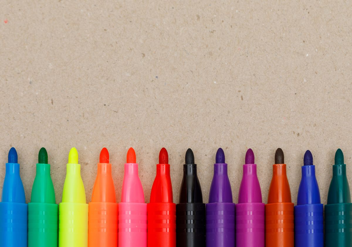 Canetinhas coloridas enfileiradas sobre uma superfície de papel, usadas para colorir livros como os da Bobbie Goods.