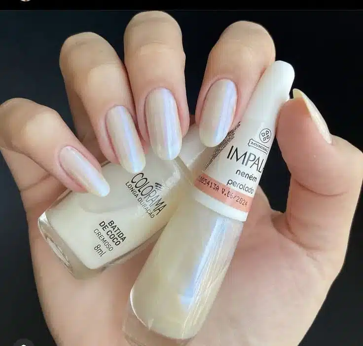 Unhas com esmalte perolado, acabamento suave e brilhante com tonalidade clara e iridescente.