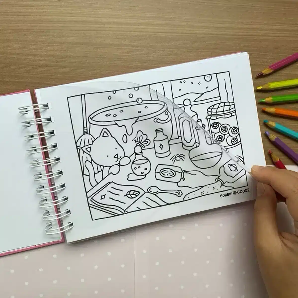 Folha de acetato sendo usada como proteção em livro de colorir Bobbie Goods com lápis ao lado