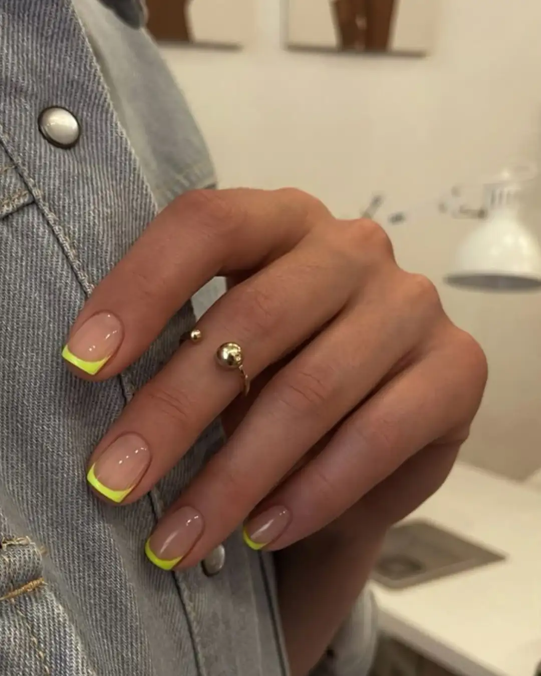 Unhas com francesinha amarelo neon e anel dourado em destaque.
