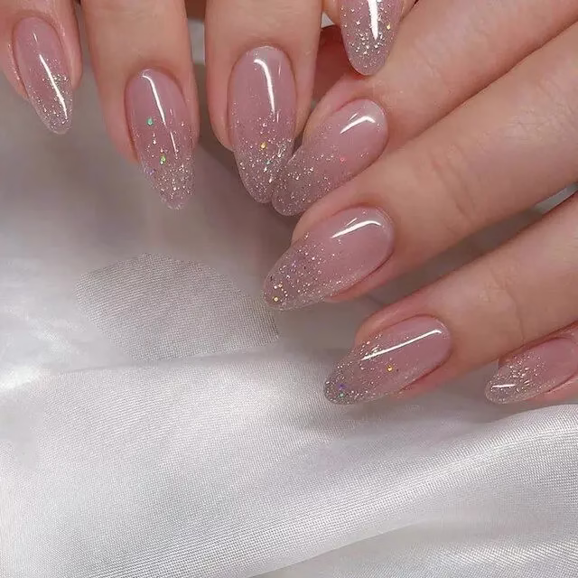Unha redonda com glitter prata e base nude, criando um efeito de brilho sutil e moderno.