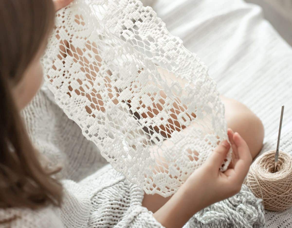Mulher segurando peça delicada de crochê feita à mão com linha clara e agulha