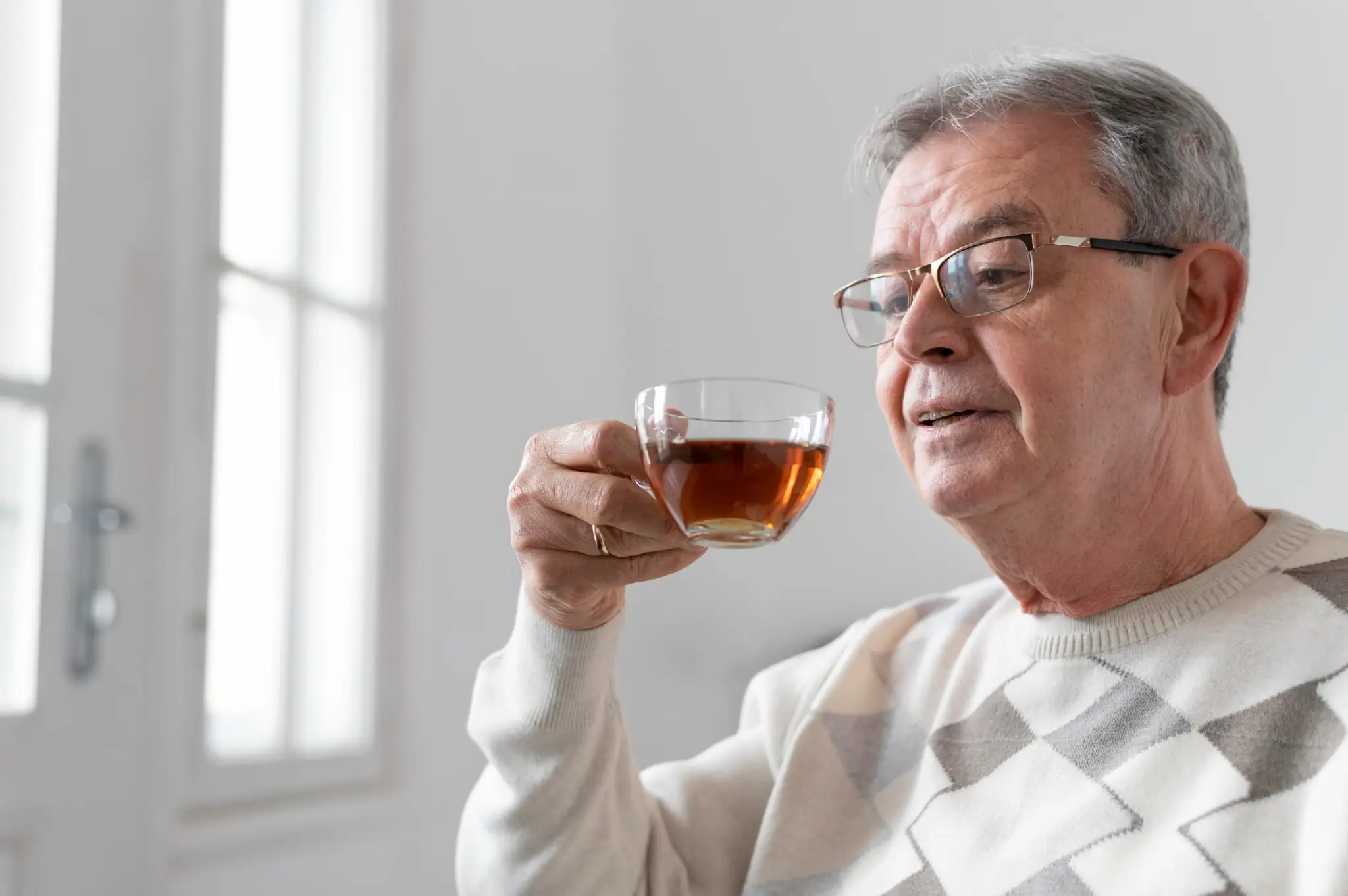 Senhor idoso apreciando uma xícara de chá em ambiente iluminado, simbolizando saúde e bem-estar na terceira idade.