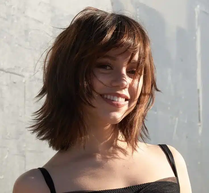 Jenna Ortega com corte de cabelo butterfly cut desfiado e com franja