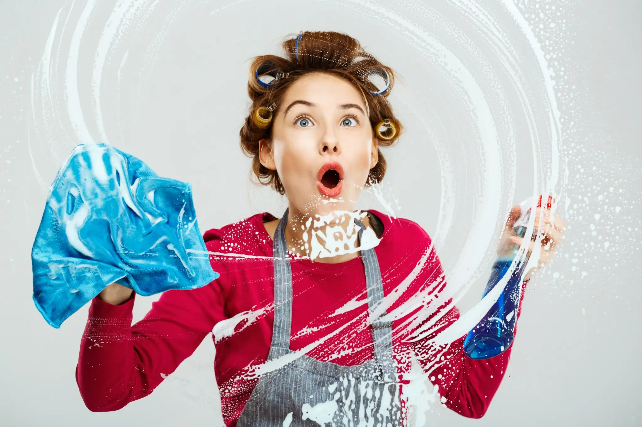 Mulher surpresa limpando vidro com pano azul e spray de limpeza.