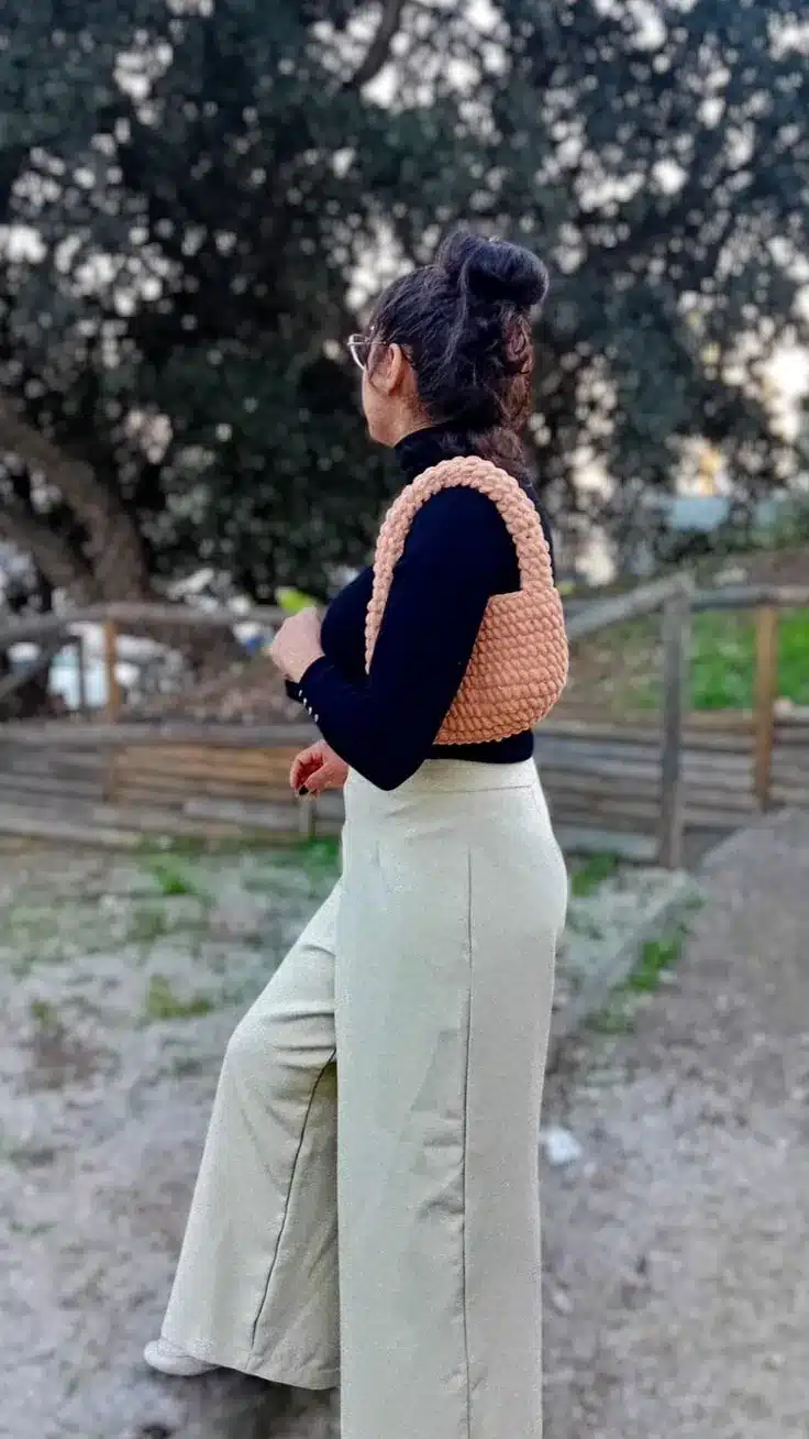 Mulher de perfil com look de inverno e bolsa de crochê rosada no ombro