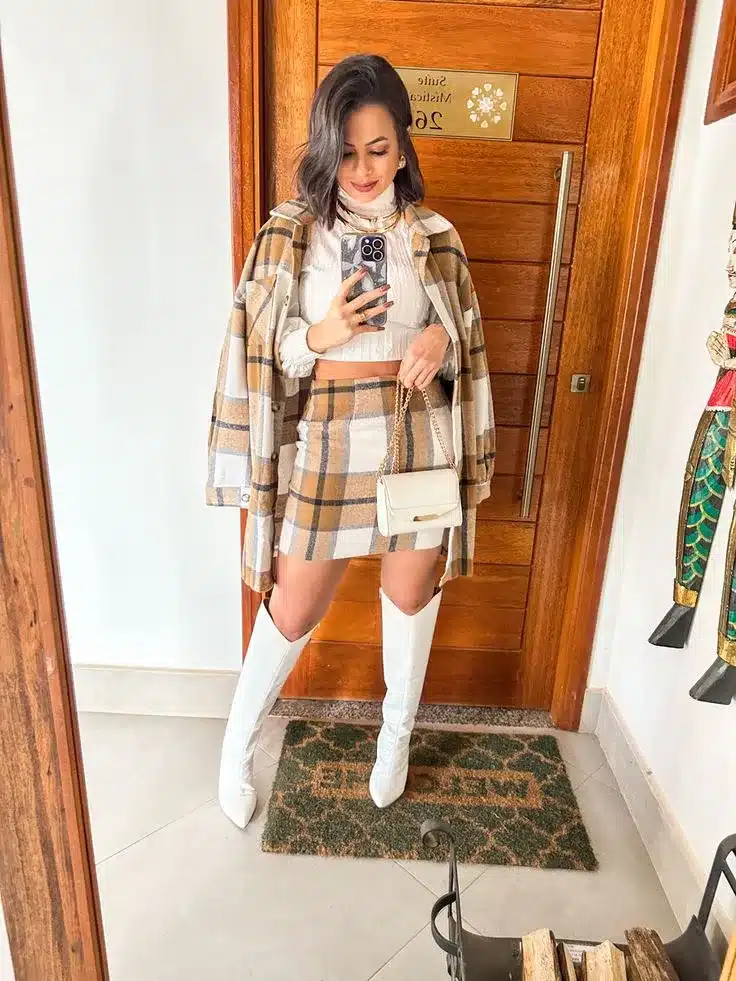 Mulher usando conjunto xadrez com saia e casaco, botas brancas de cano alto e bolsa branca