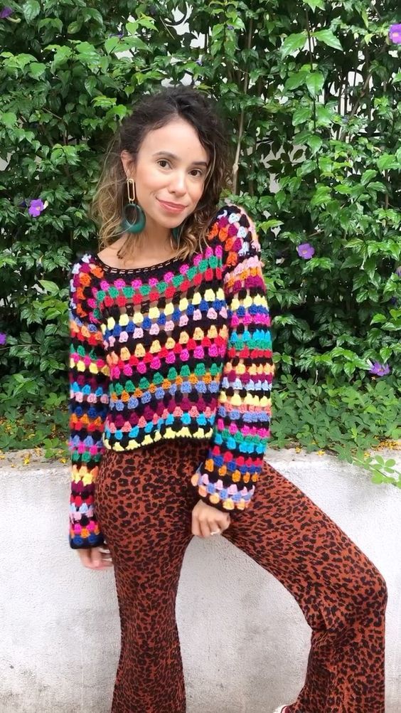 Mulher usando blusa de crochê colorida com pontos fechados e calça estampada, em ambiente ao ar livre
