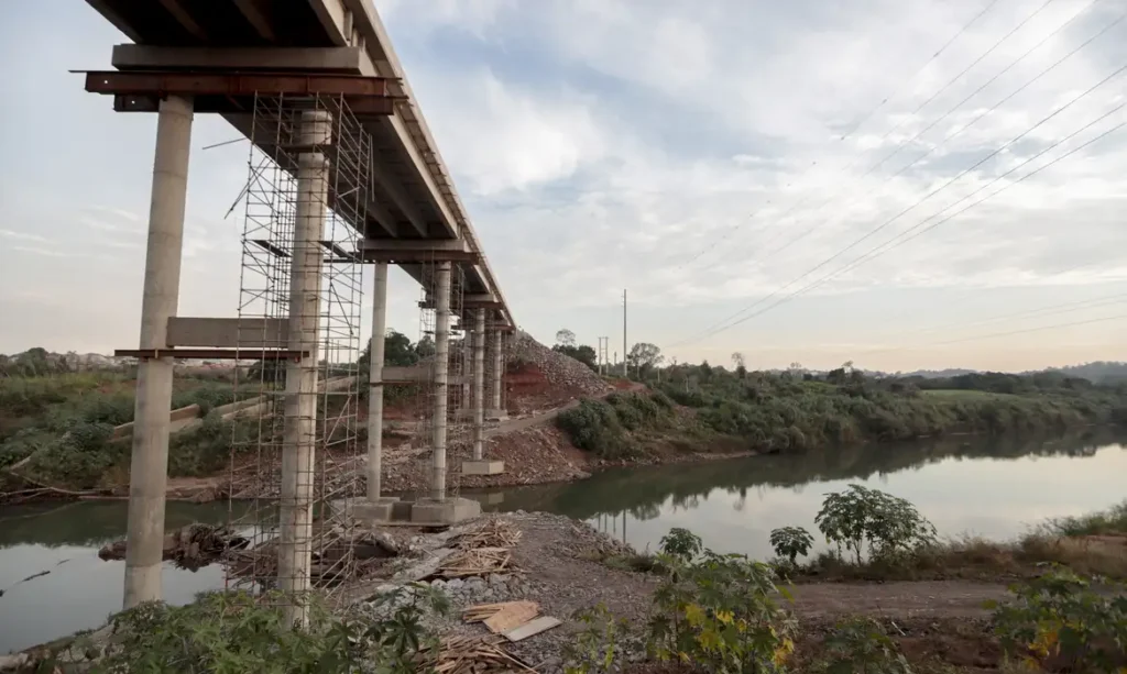 Obra de ponte em construção sobre rio, com estrutura de concreto e andaimes
