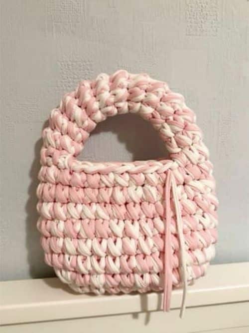 Mini bolsa de crochê em tons de rosa e branco, com alça arredondada.