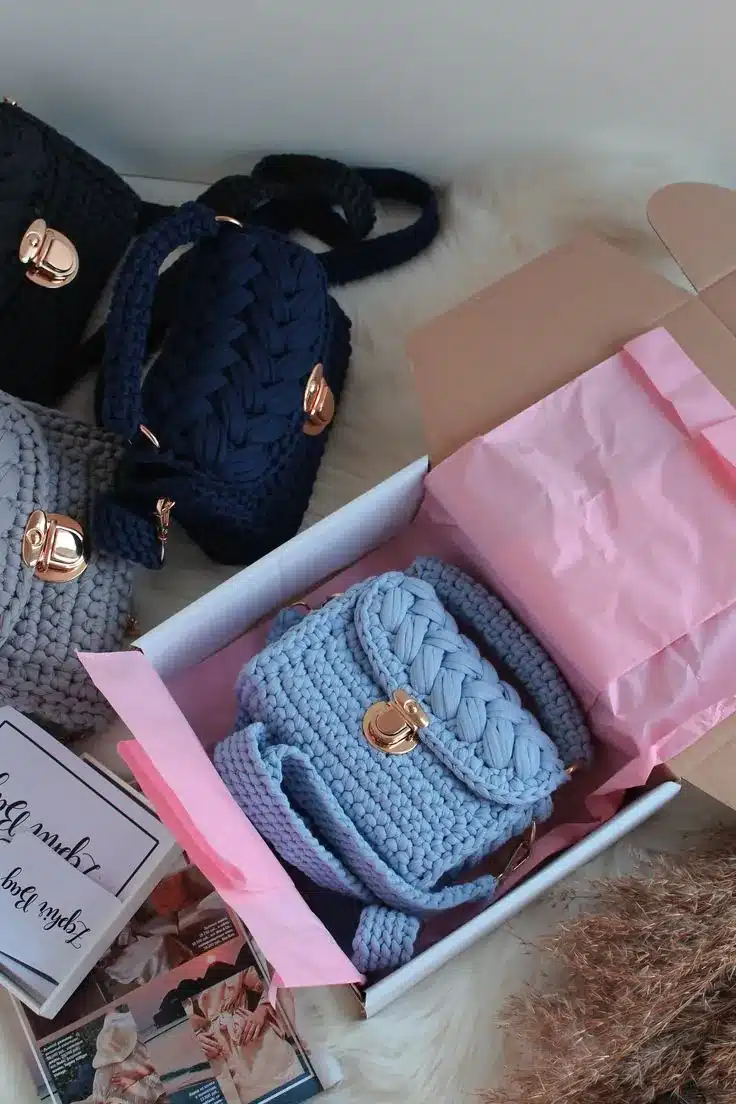 Mini bolsas de crochê coloridas com fecho dourado, uma delas em caixa de presente