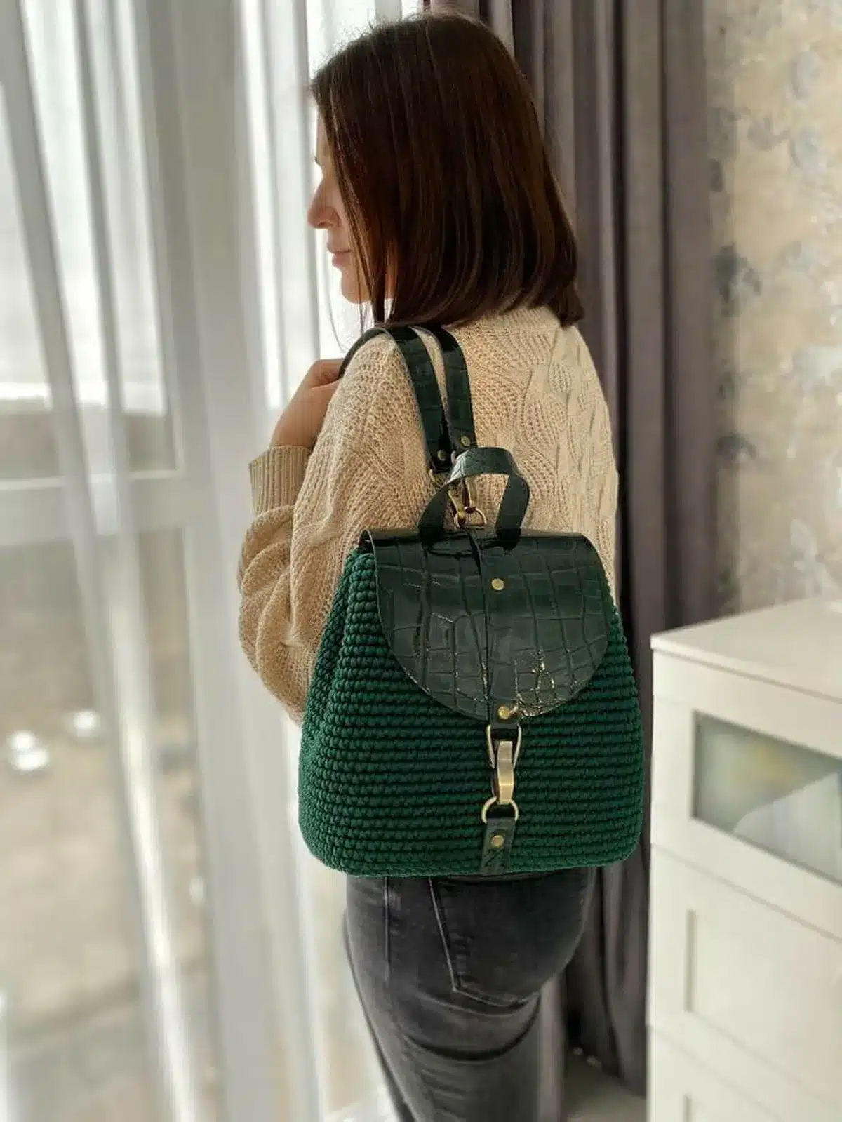 Mochila de crochê verde com detalhes em couro, usada por mulher de cabelo curto em ambiente interno