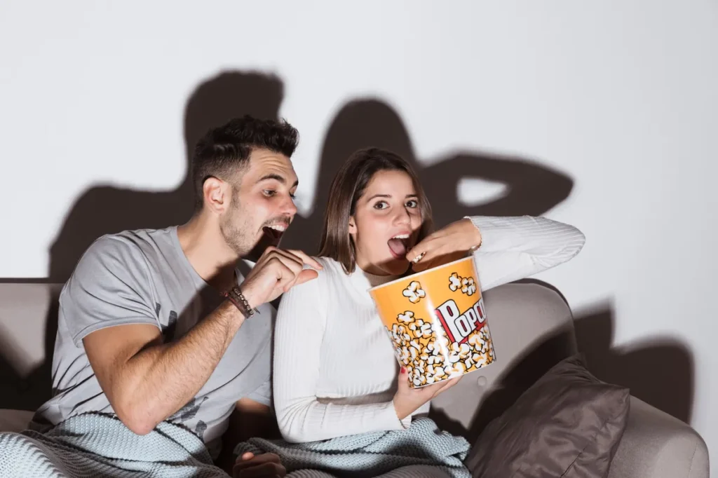 Casal assistindo filme no sofá comendo pipoca em noite aconchegante em casa