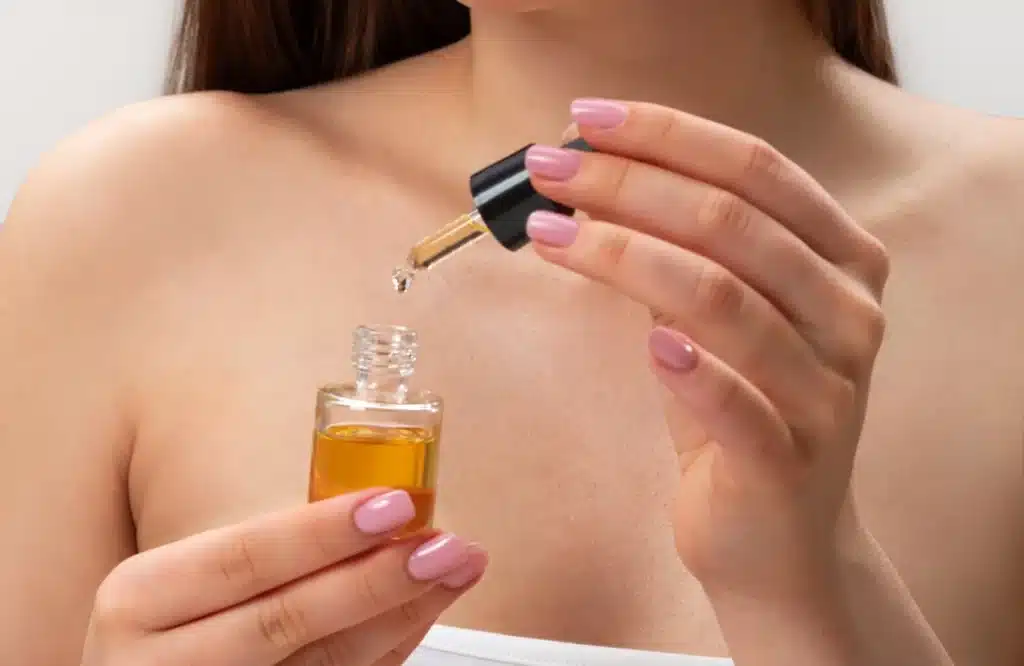 Mulher com unhas feitas aplicando óleo secante em conta-gotas