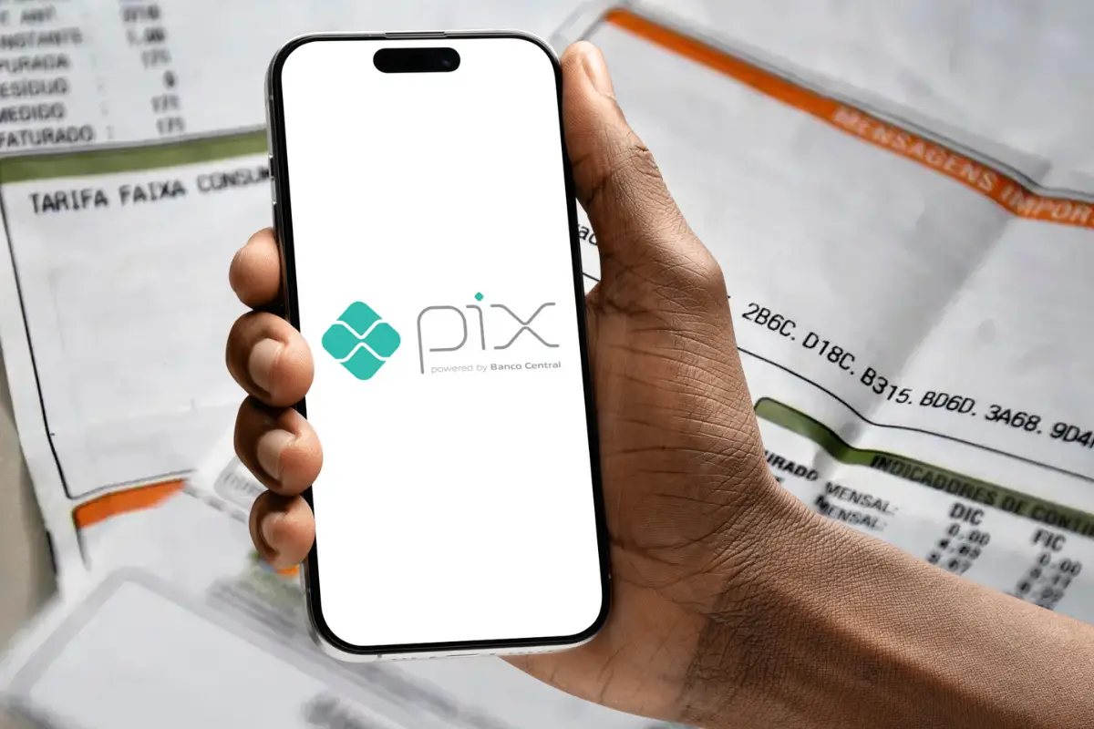 Pessoa segurando celular com o logo do Pix na tela e contas ao fundo´.