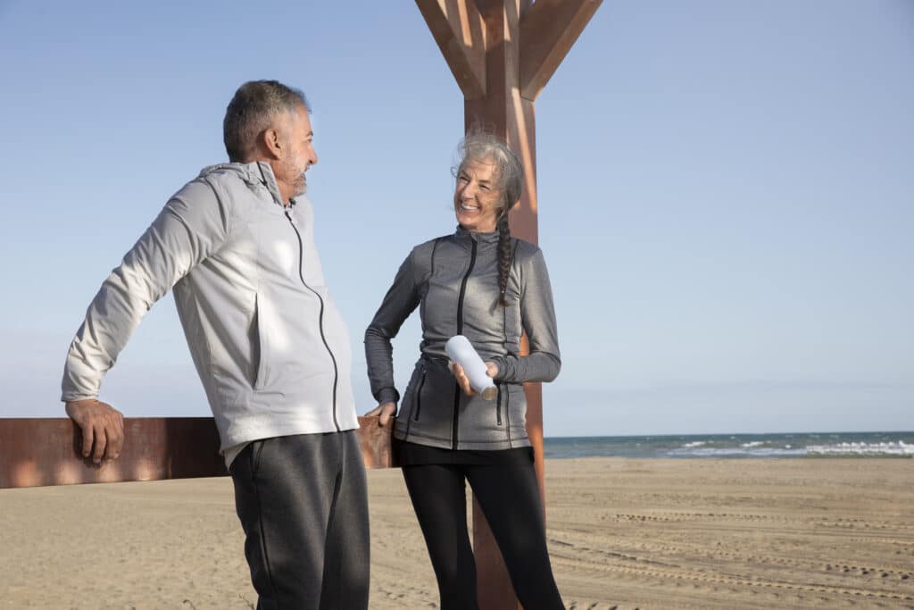 Casal maduro se exercitando e sorrindo na praia, representando vitalidade e bem-estar