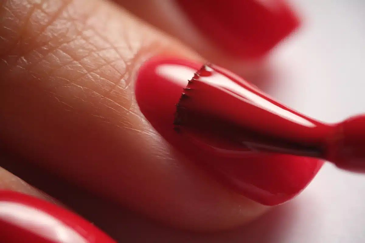 Aplicação precisa de esmalte vermelho vibrante em unha.