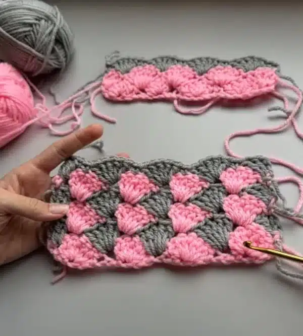 Ponto concha em crochê com cores rosa e cinza, mostrando a técnica de pontos altos e baixos formando um padrão de conchas.