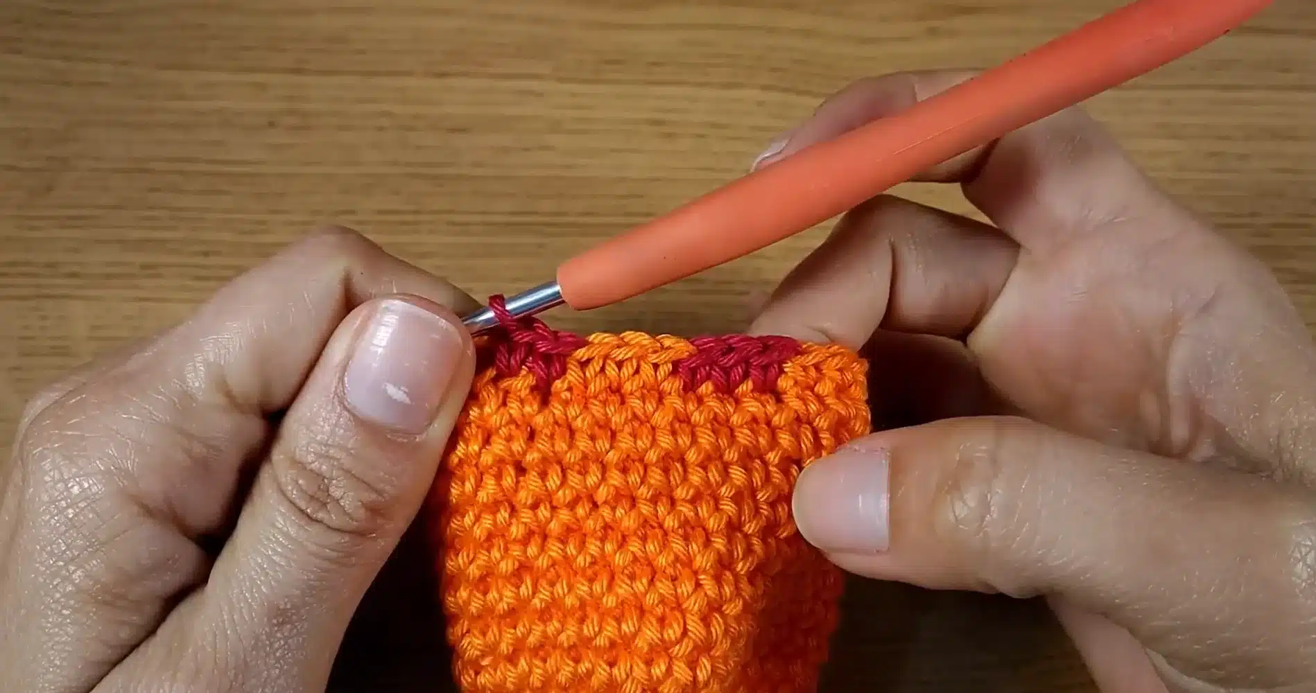 Detalhe da finalização de troca de cores com ponto baixo em crochê, mostrando as mãos e o fio de trabalho.