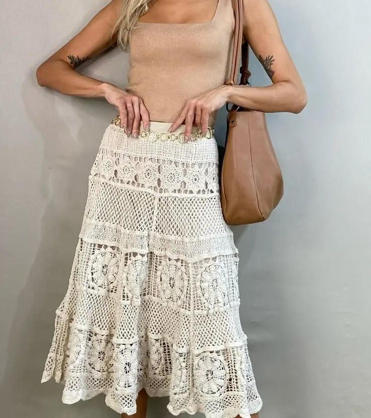 Mulher usando saia de crochê estruturada com blusa lisa e bolsa de couro.