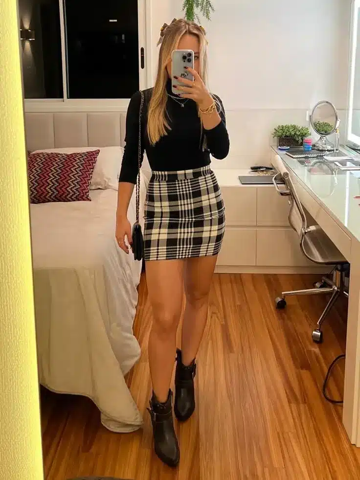 Mulher usando blusa preta e saia xadrez preta e branca, com botas de couro