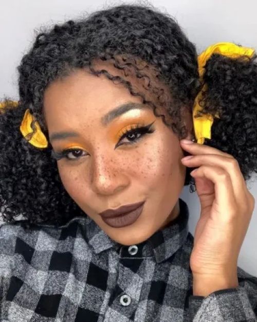 Mulher com maquiagem junina, usando penteado com fitas amarelas e pintinhas na pele, inspirada para festas de São João.