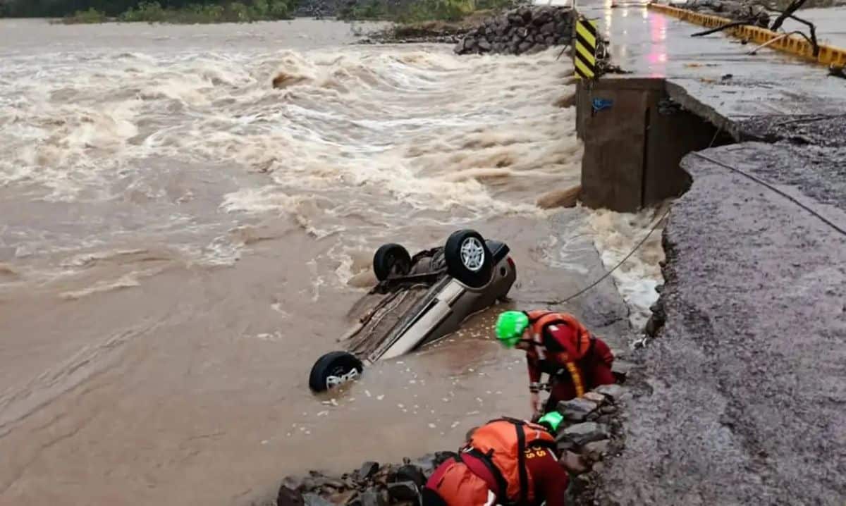 Equipe de resgate atua em área alagada com carro submerso após rompimento de estrada