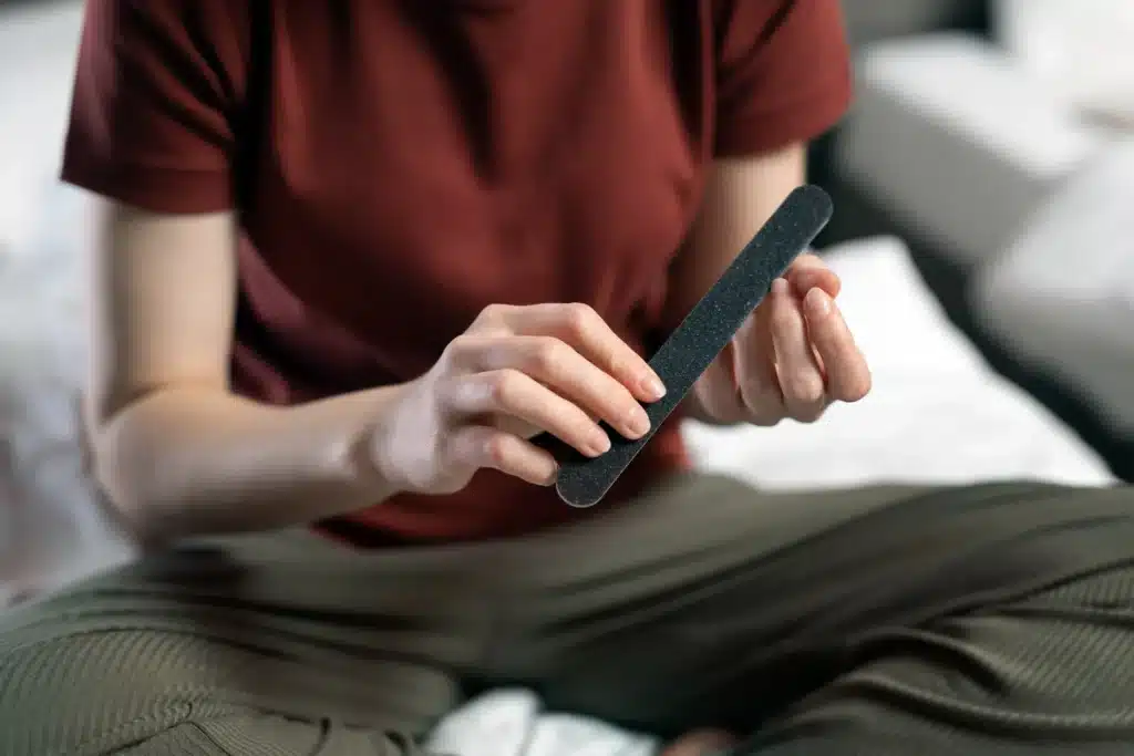 Pessoa lixando as unhas em casa, cuidando do comprimento ideal para evitar quebras.