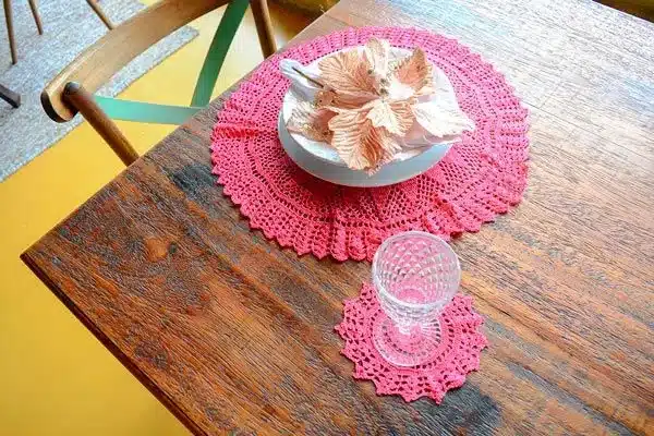 Toalha de crochê rosa com porta-copo decorando mesa de madeira rústica