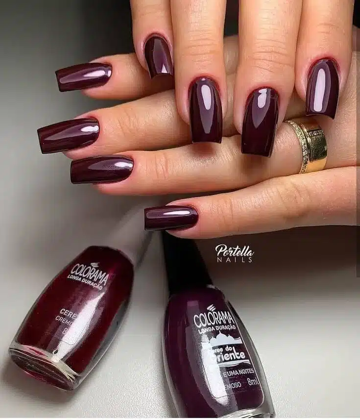 Unhas em tons escuros de vinho, com acabamento brilhante, transmitindo modernidade e força.