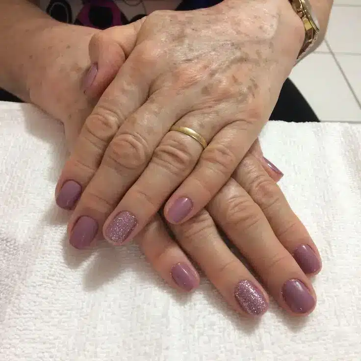 Unhas de mulher madura decoradas com esmalte roxo e glitter
