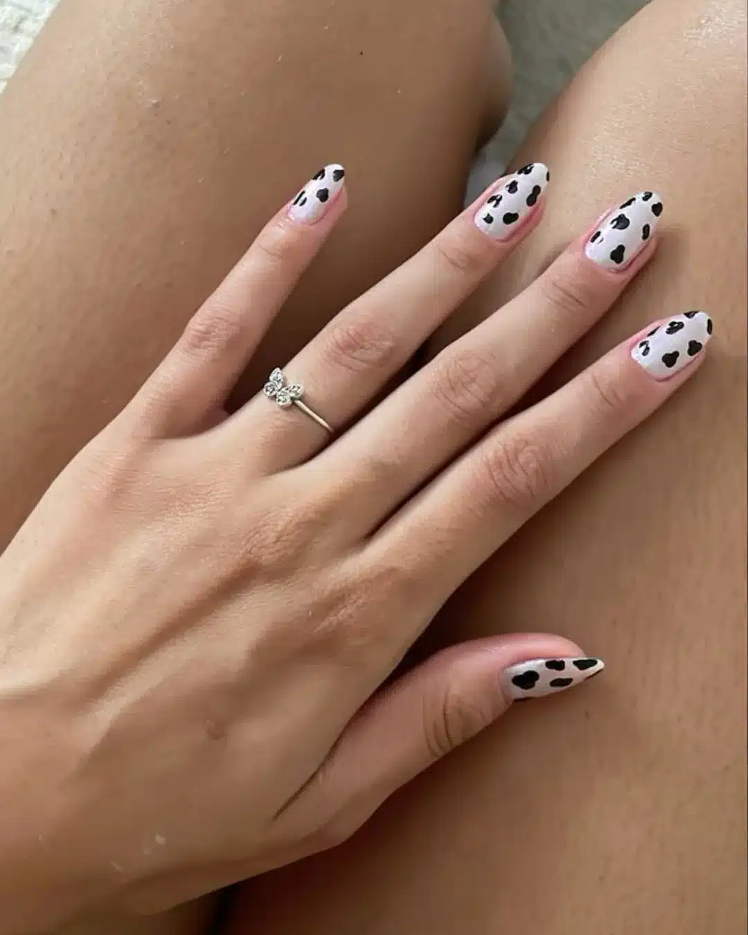 Unhas decoradas com estampa de vaca sobre base rosa clara.