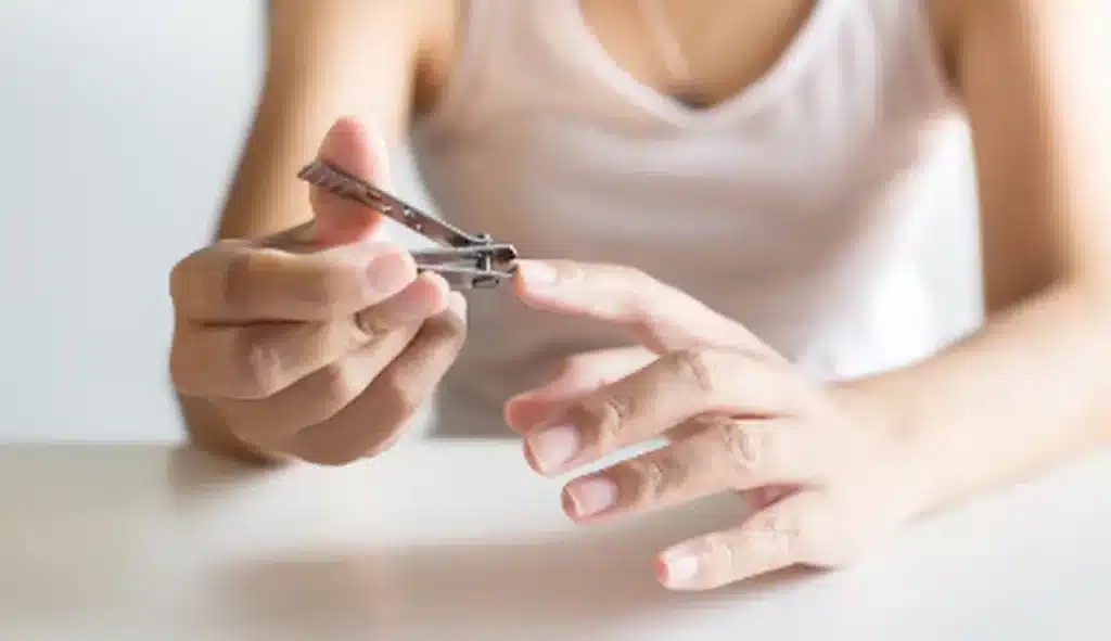 Pessoa cortando as unhas com um cortador de unha, em ambiente com foco na ação de cuidados pessoais.