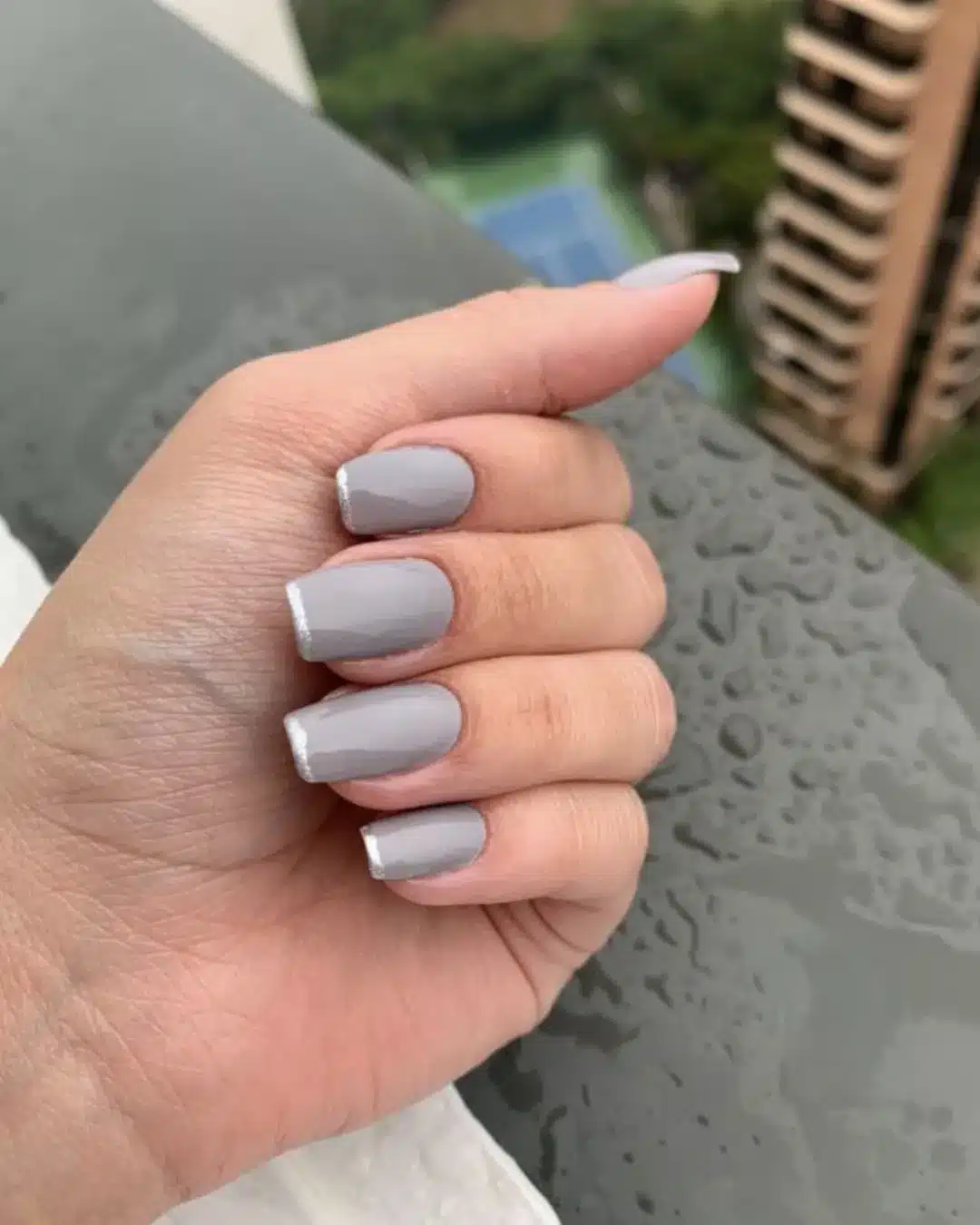 Unhas pintadas com esmalte cinza fosco e bordas brancas.