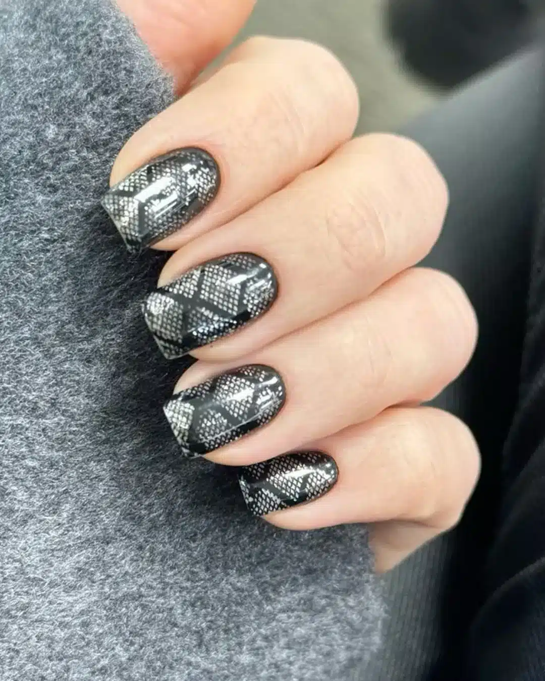 Unhas com esmalte preto decorado com estampa metálica imitando pele de cobra.