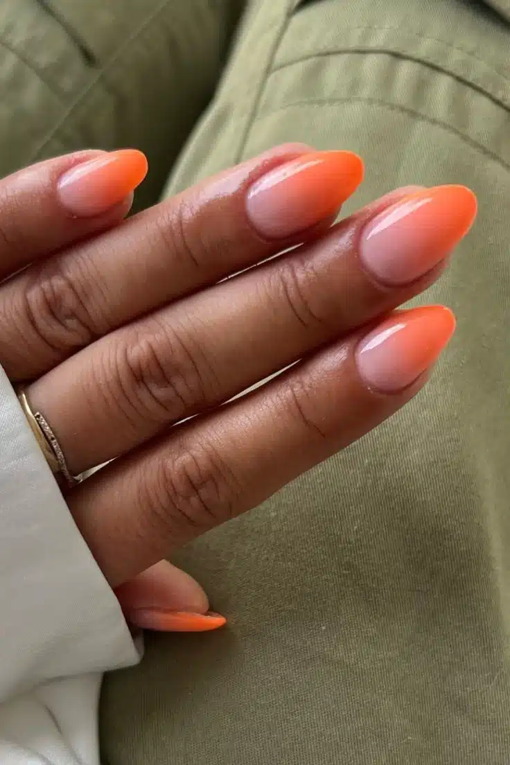 Unhas com esmalte ombré em tons de laranja, criando efeito degradê vibrante.